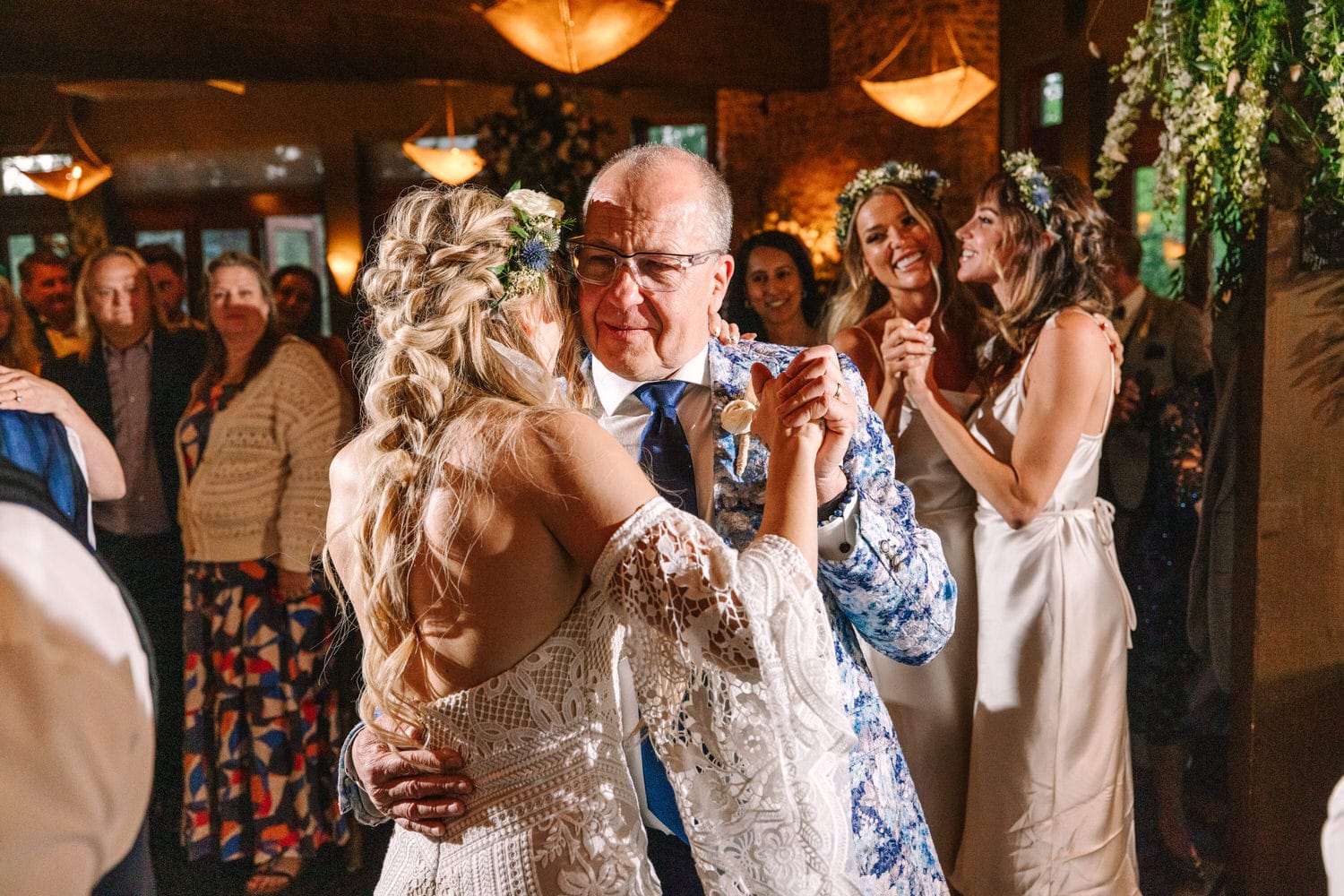 A heartfelt moment of a father dancing with his daughter during their wedding reception, surrounded by joyful guests and warm lighting.