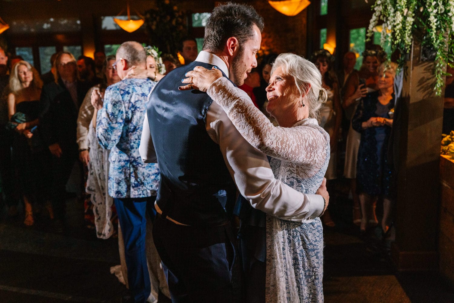 A man and woman share a joyful dance surrounded by friends and family, embodying a moment of love and connection at a celebratory event.