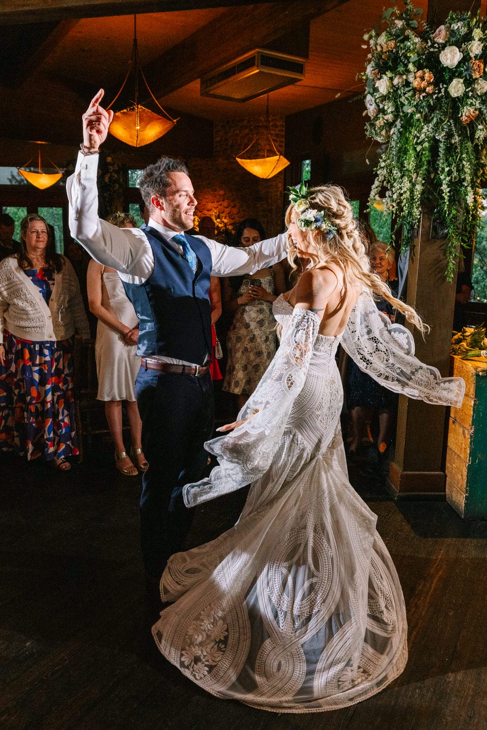 A joyful couple dances at their wedding reception, surrounded by smiling guests in an elegantly decorated venue.