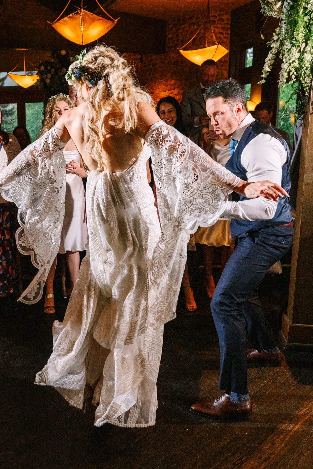 A couple dances joyfully during a wedding reception, surrounded by smiling guests in a beautifully decorated venue.