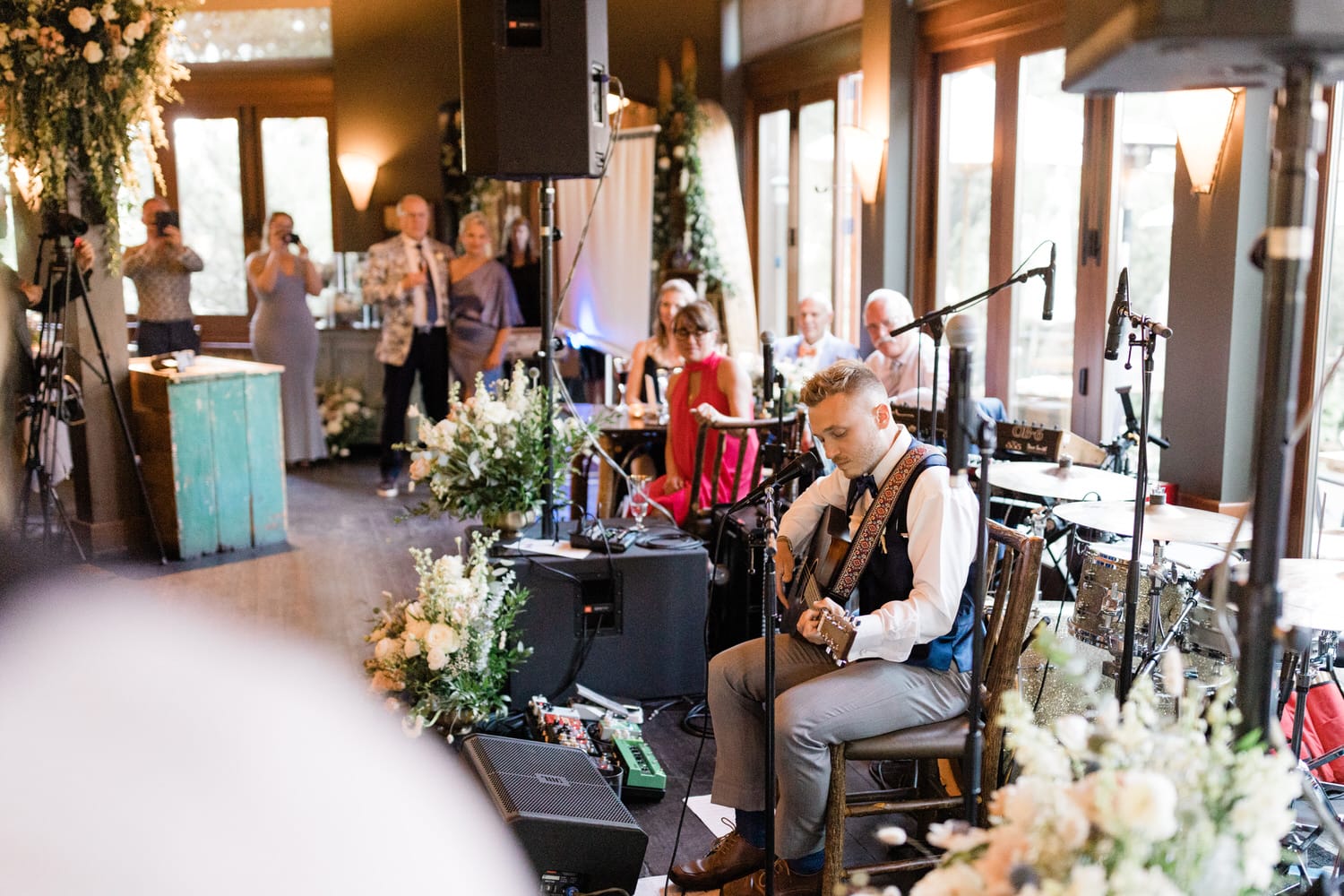 A musician plays guitar for an audience at a beautifully decorated venue with floral arrangements and an inviting atmosphere.