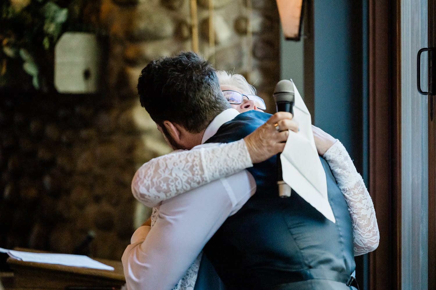 A heartfelt hug between a man in a formal outfit and a woman in a lace dress, capturing a moment of joy and connection during a special event.