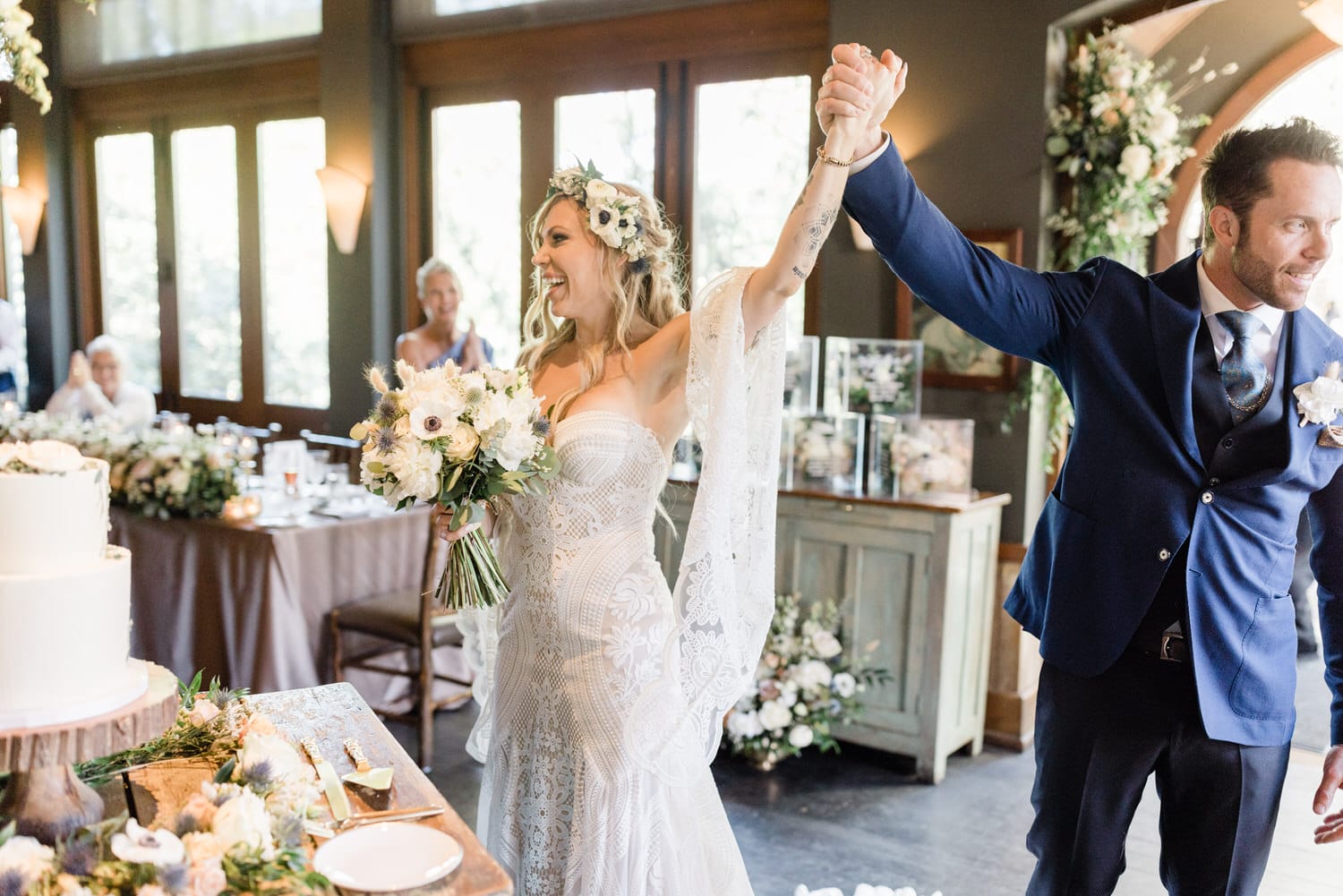 A joyful couple raises their arms in celebration, surrounded by elegant decor and a wedding cake as they embrace their new life together.