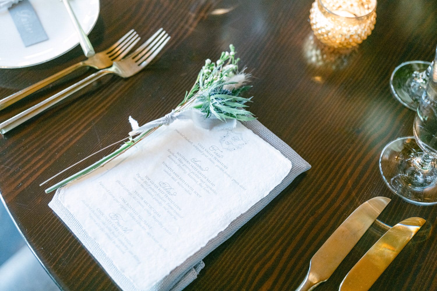 A beautifully arranged dining table featuring a menu with delicate floral decor, golden utensils, and soft candlelight.