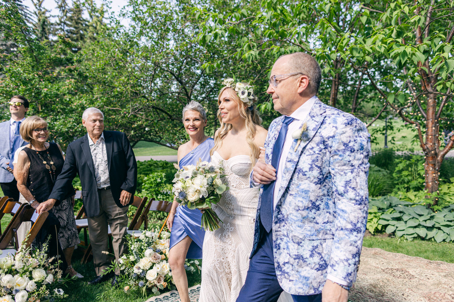 A joyful bride walks down the aisle with her parents, surrounded by lush greenery and floral arrangements, capturing a moment of love and celebration.