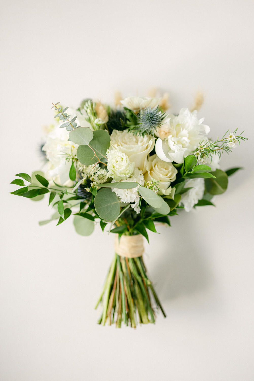 A beautifully arranged bouquet featuring white flowers, greenery, and accents of blue thistles against a soft background.