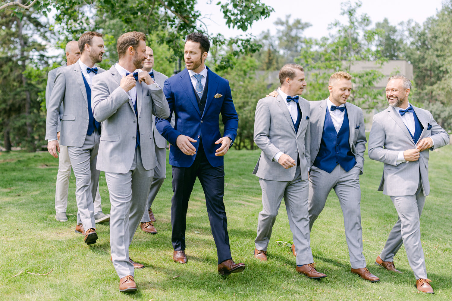 A group of well-dressed men in suits walking together in a lush outdoor setting, showcasing camaraderie and style.