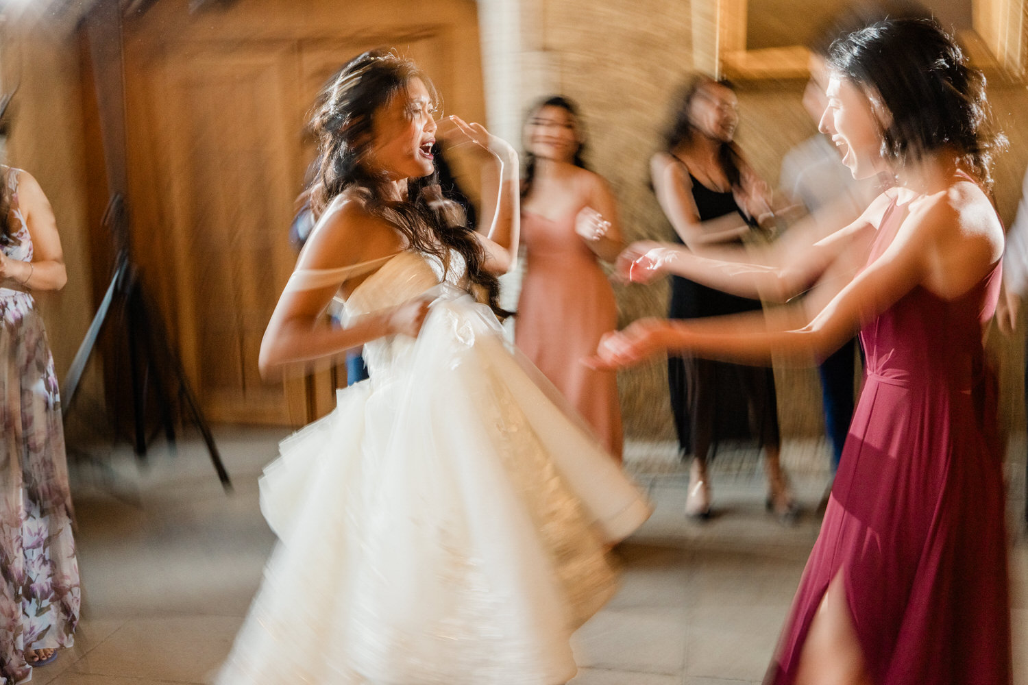 Two women dancing energetically at a lively event, surrounded by friends in a festive atmosphere.