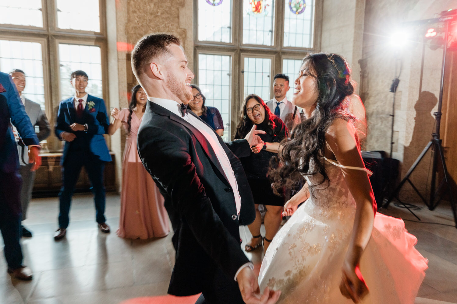 A couple enjoying a lively dance at their wedding reception, surrounded by smiling guests in a beautifully lit hall.