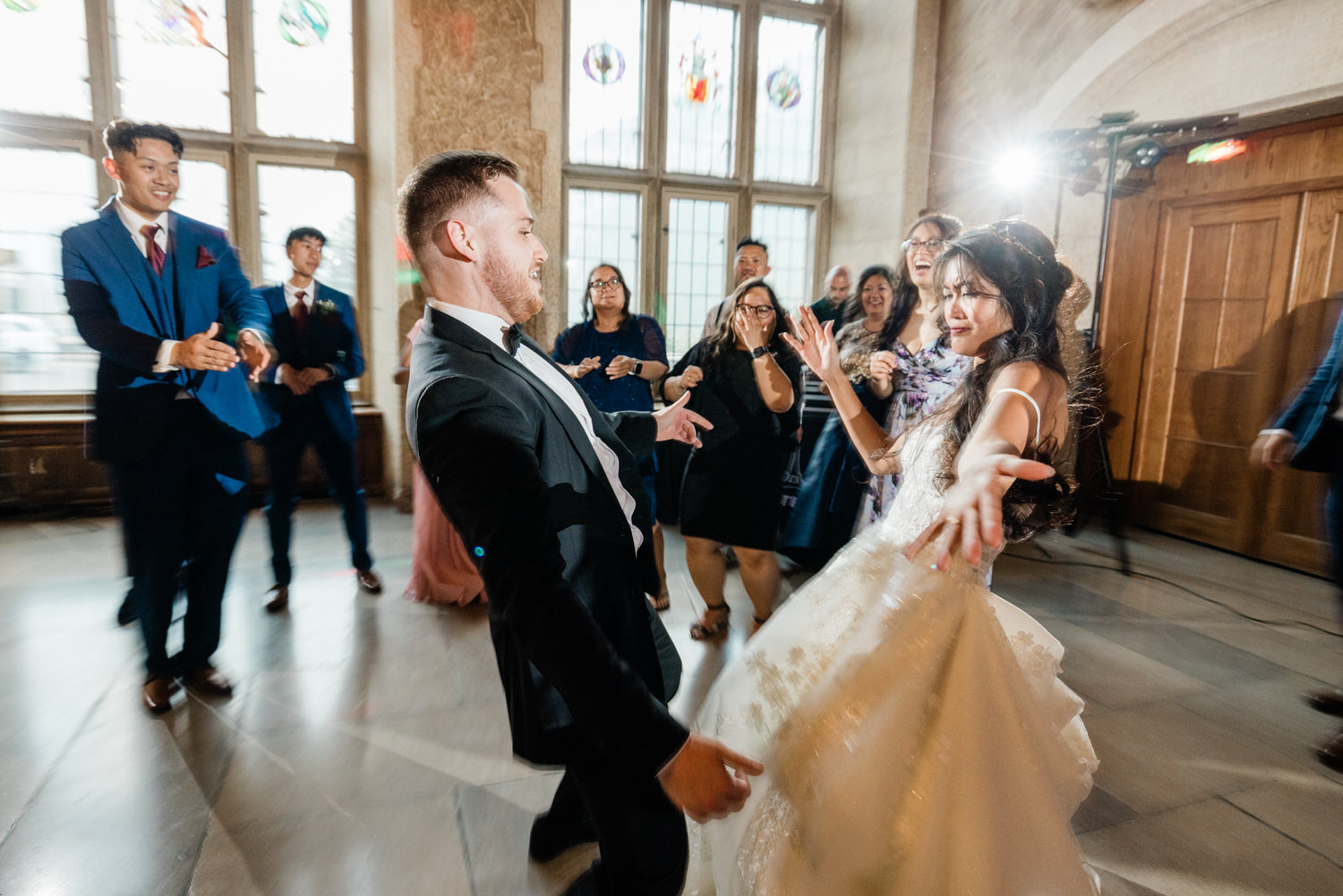 A joyful wedding reception scene with the bride and groom dancing together, surrounded by friends and family, all enjoying the moment. Bright stained glass windows and a lively atmosphere enhance the festive spirit.