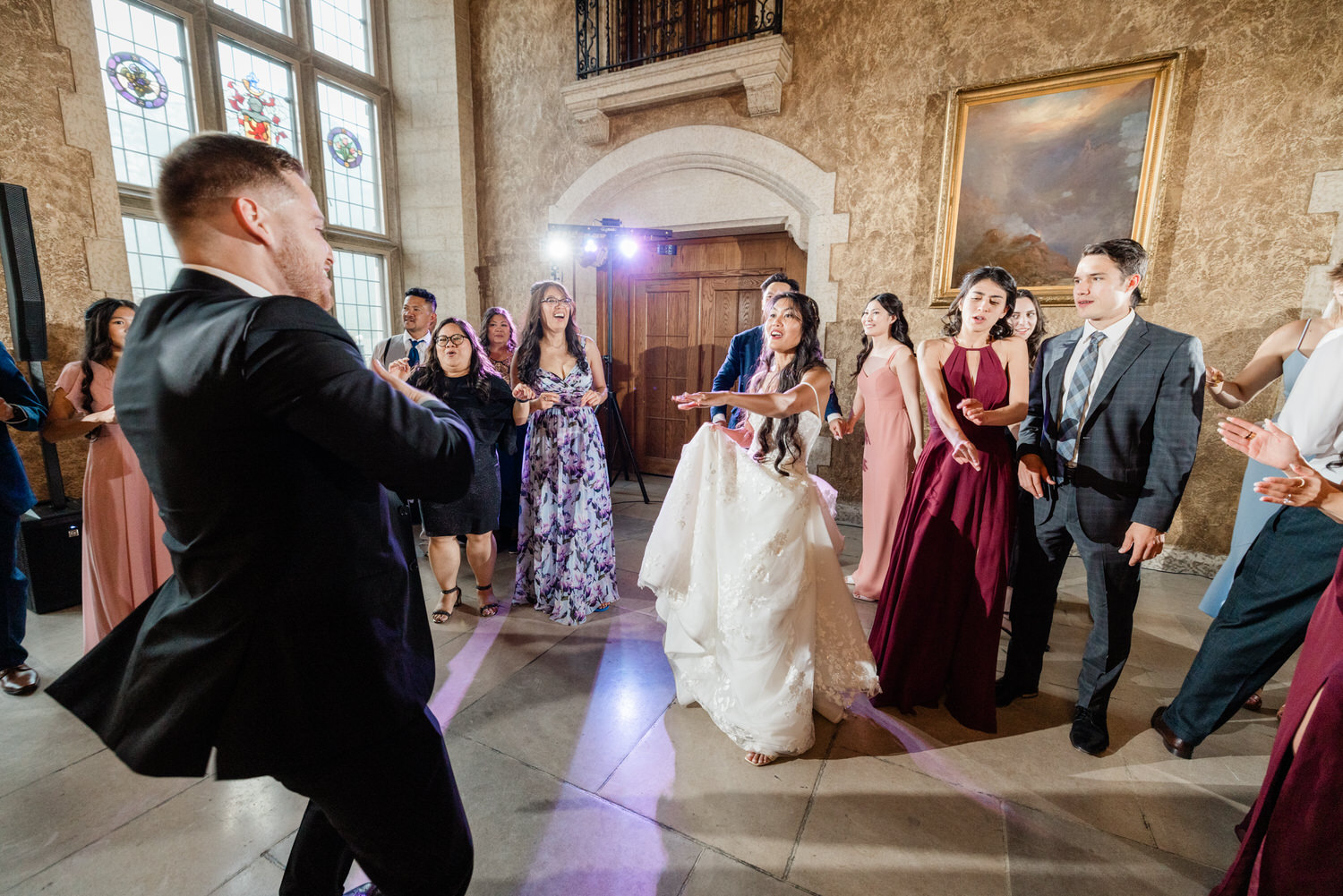 A lively group of guests dancing joyfully at a wedding reception, with the bride in a beautiful white gown in the foreground and a festive atmosphere highlighted by elegant decor.