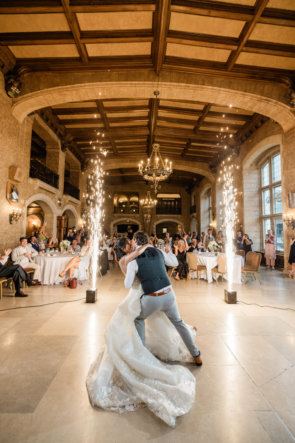 A newlywed couple shares a romantic dance surrounded by guests, with sparkling effects enhancing the festive atmosphere in an elegant venue.