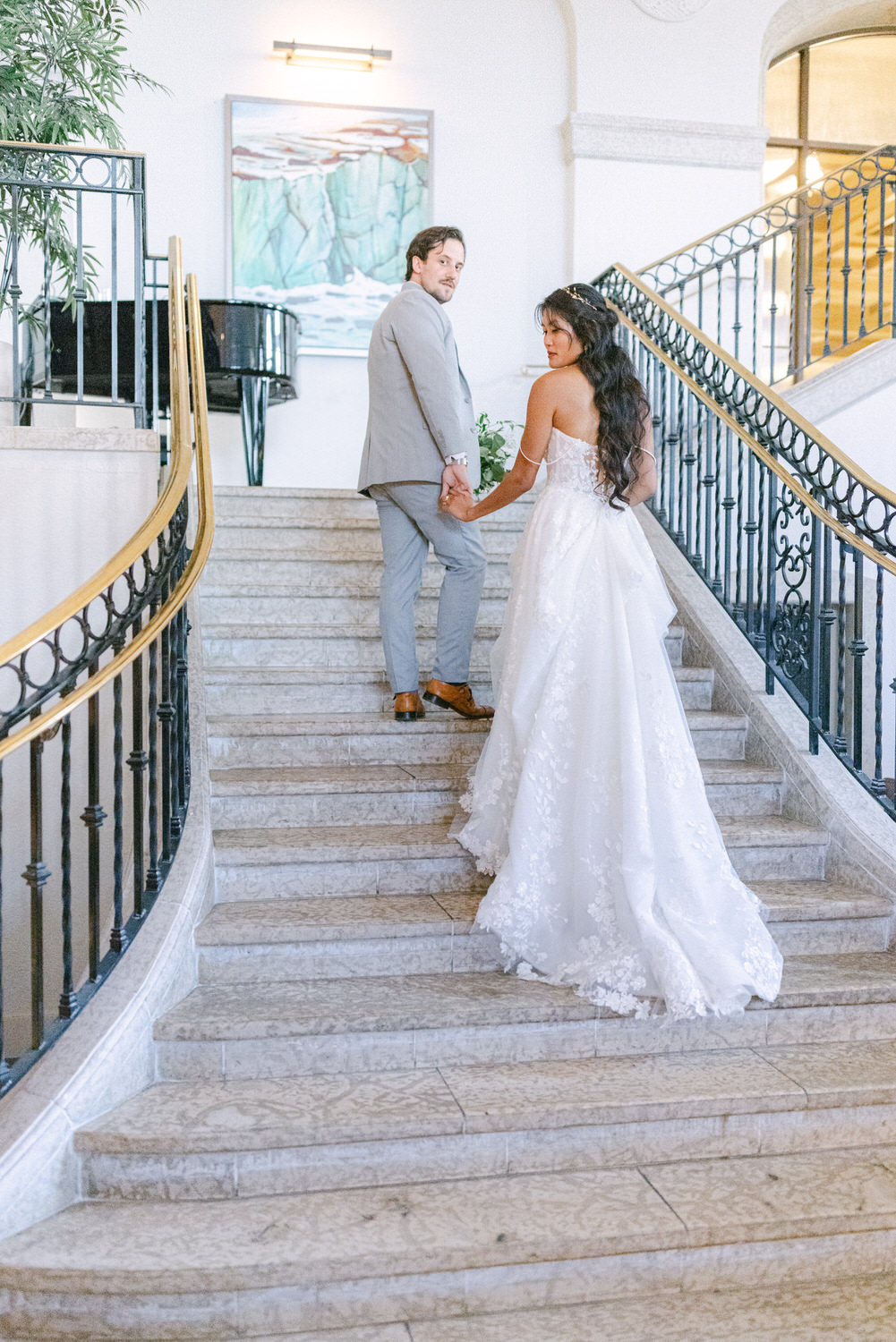 A bride and groom holding hands while ascending a staircase in a beautifully decorated venue, showcasing their joyful connection.