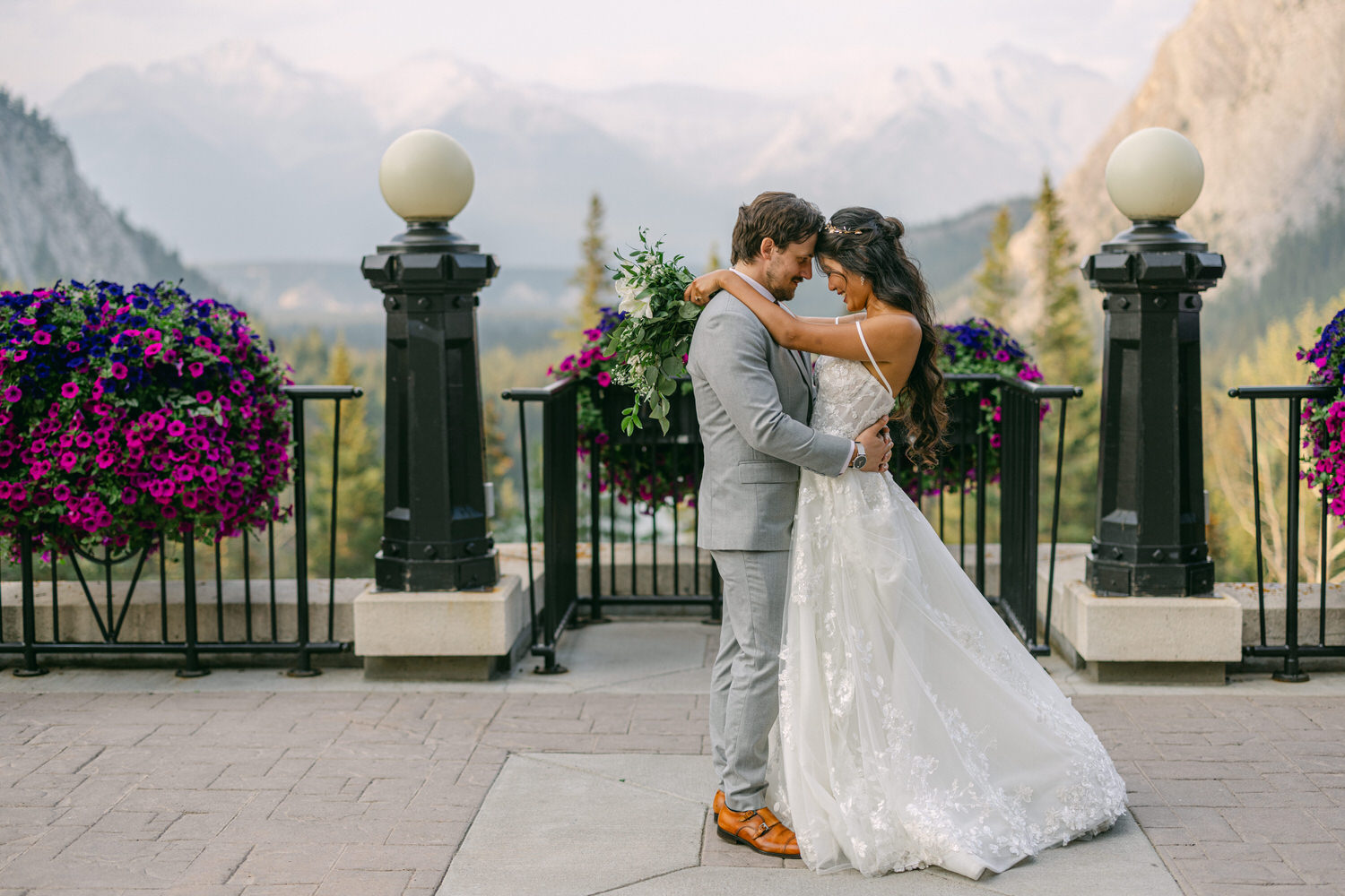 A couple shares a loving embrace in front of a stunning mountain backdrop, adorned with colorful flowers and greenery, during their wedding ceremony.