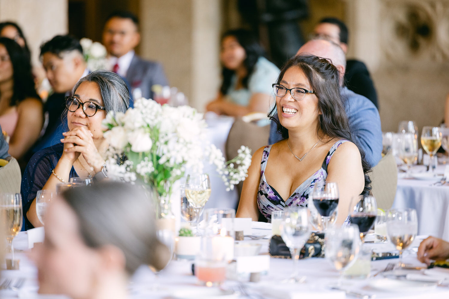 Guests enjoying a festive meal, with laughter and conversation amidst elegantly arranged tables and floral centerpieces.