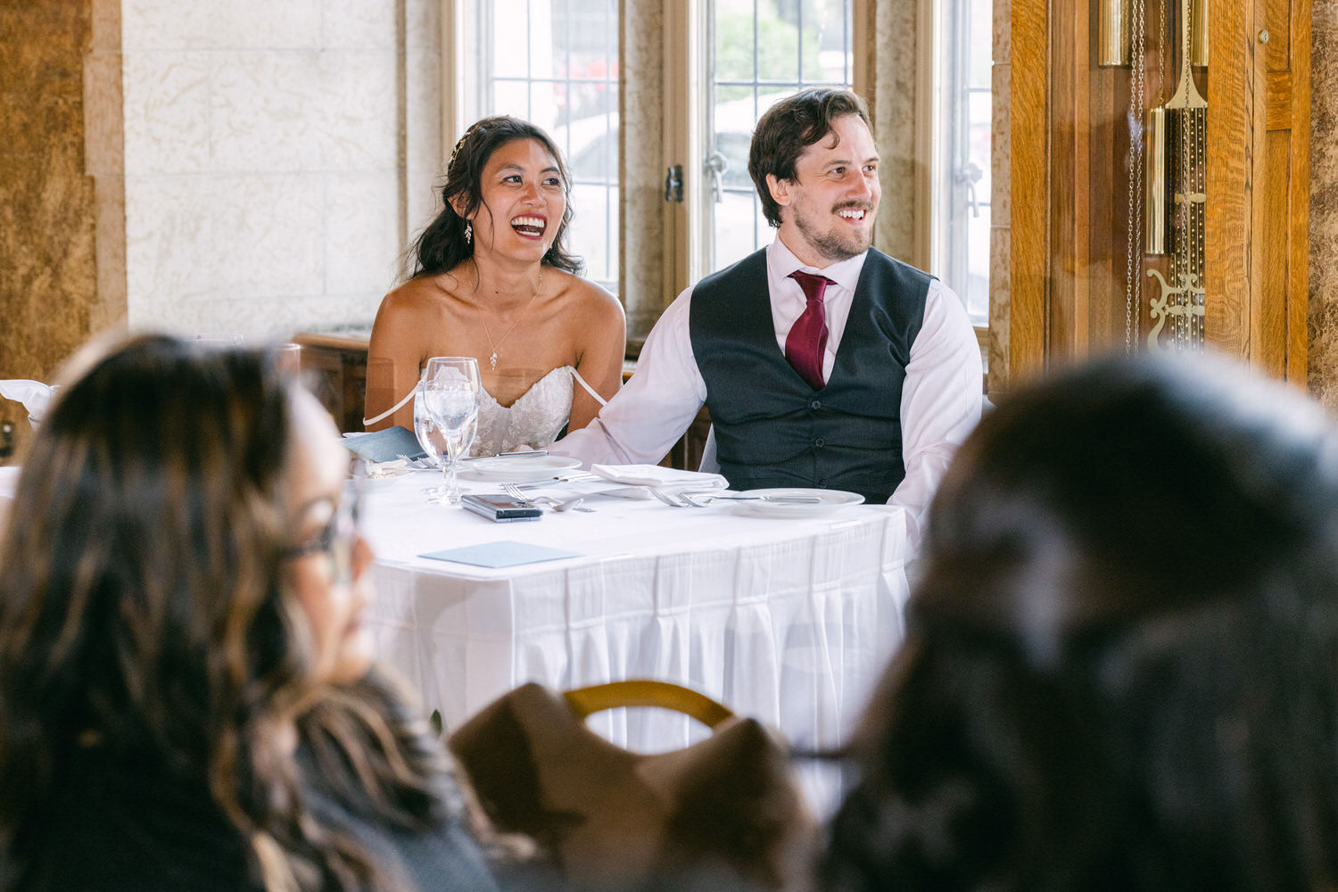 A happy bride and groom share a lighthearted moment while seated at a beautifully set table, surrounded by guests.