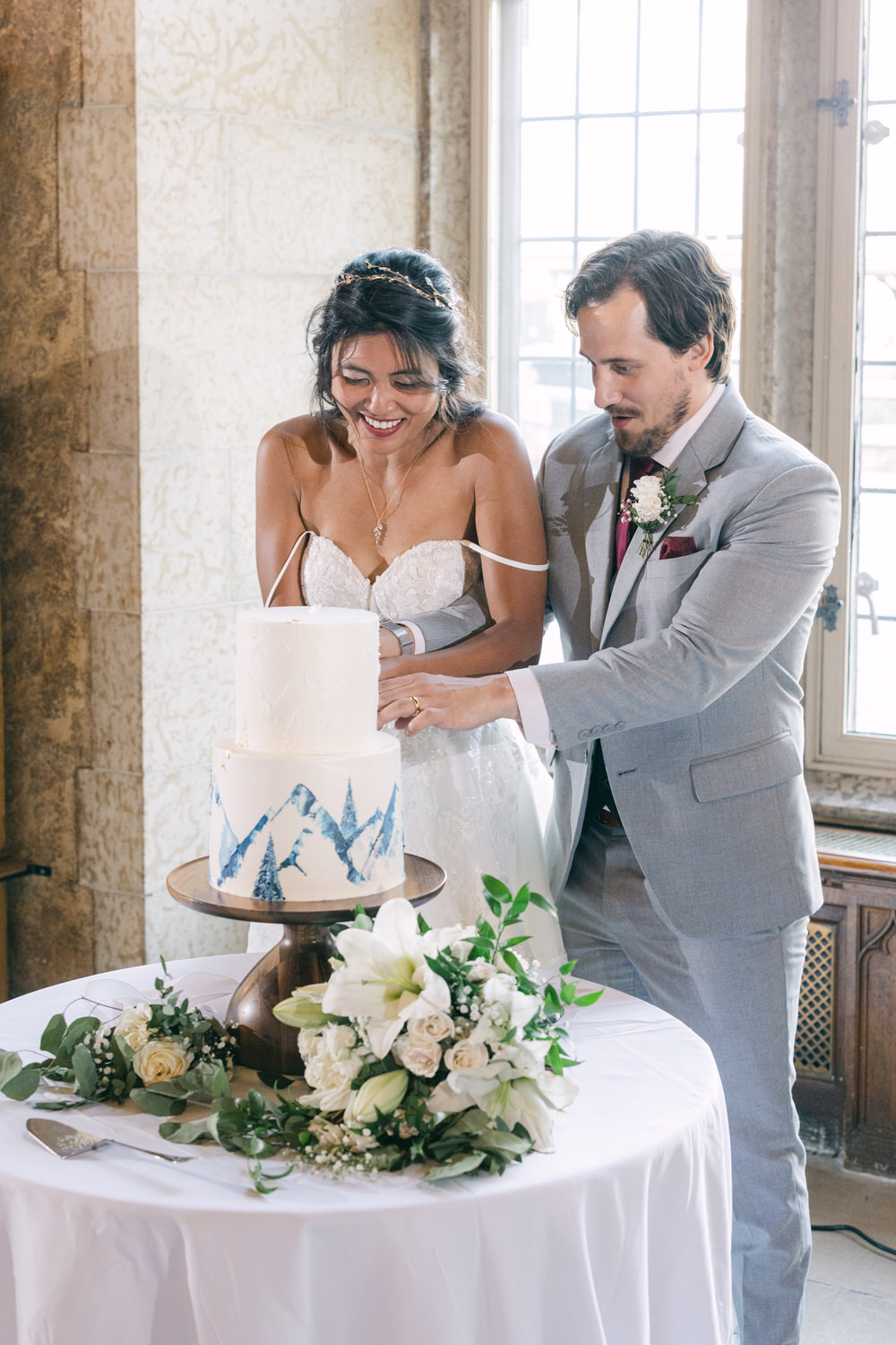 A joyful couple cuts their wedding cake together, surrounded by elegant decorations and a beautiful bouquet of white flowers.