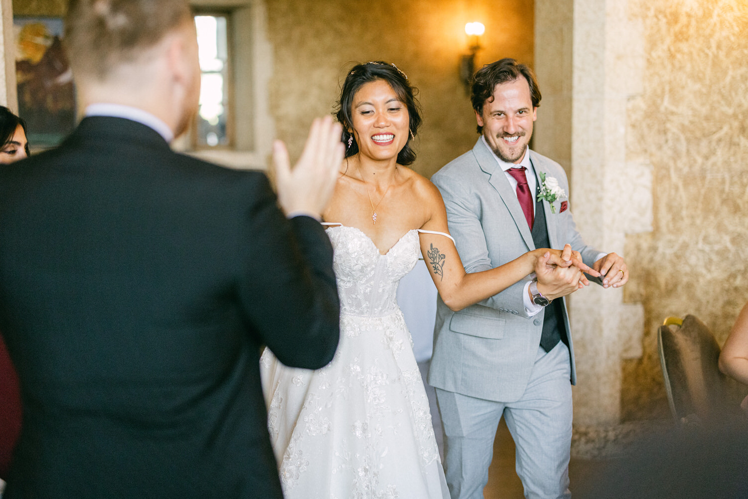 A couple smiling and dancing as they are welcomed by guests during their wedding reception, set in an elegant indoor venue.