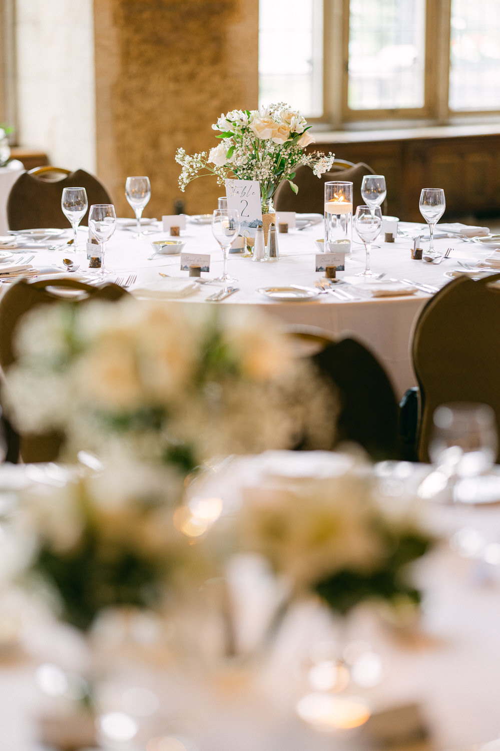 A beautifully arranged dining table featuring sparkling glassware, white table linens, and a floral centerpiece with roses and baby's breath, set for an event.