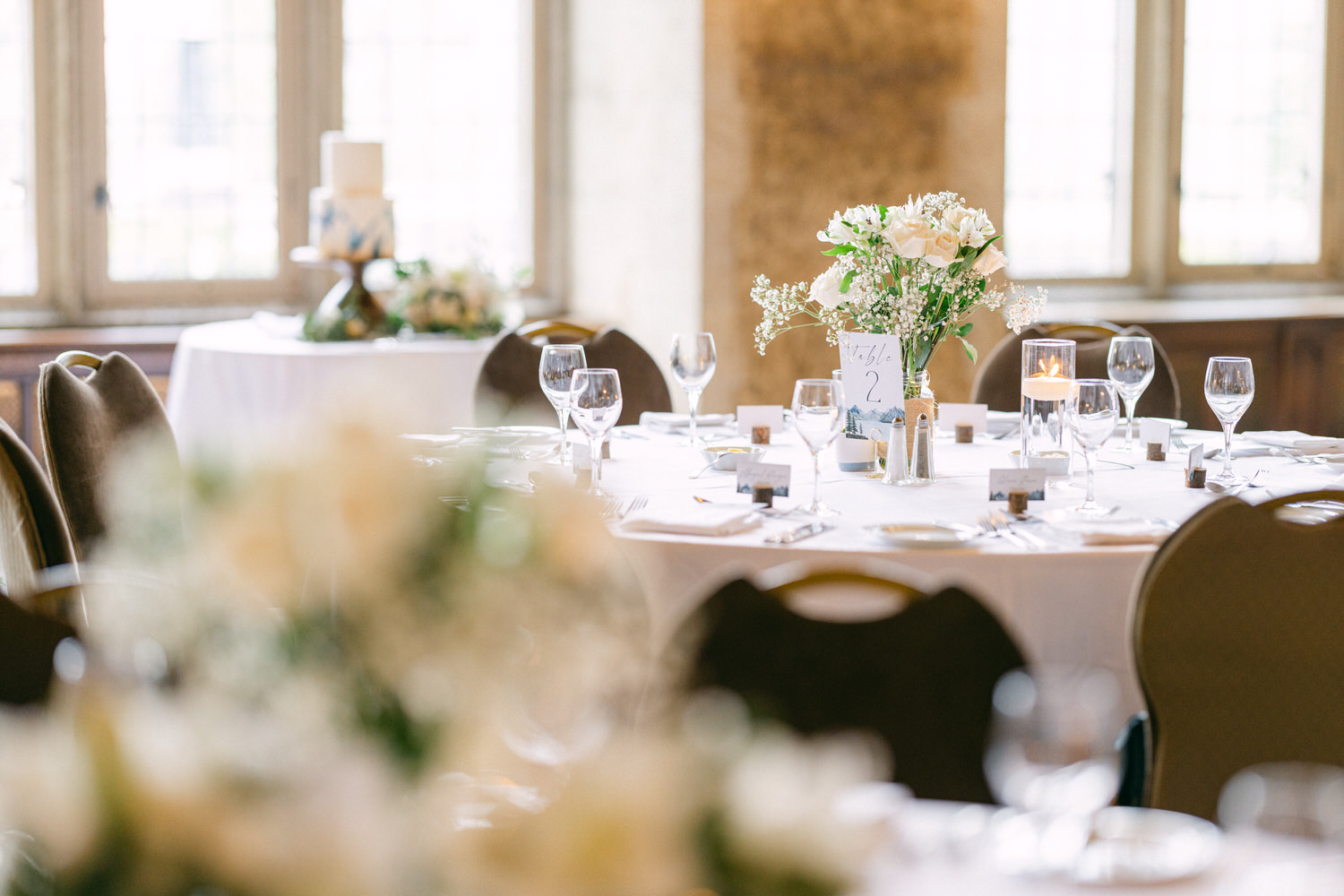 A beautifully arranged wedding table featuring white flowers, wine glasses, and intricate place settings, with a centerpiece displaying a table number and candles.