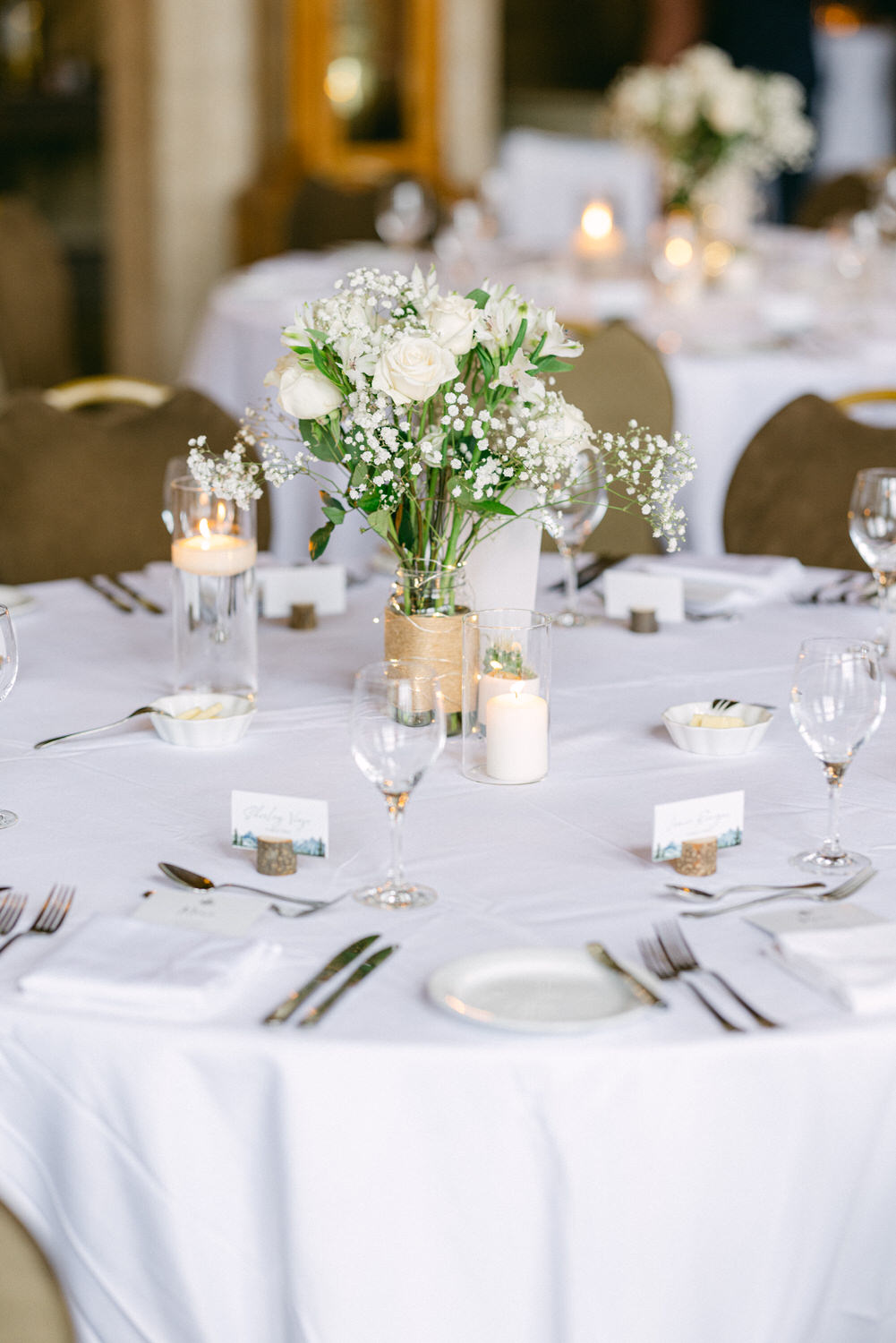 A beautifully arranged dining table featuring white roses, candles, and place cards on a white tablecloth, creating a romantic ambiance.