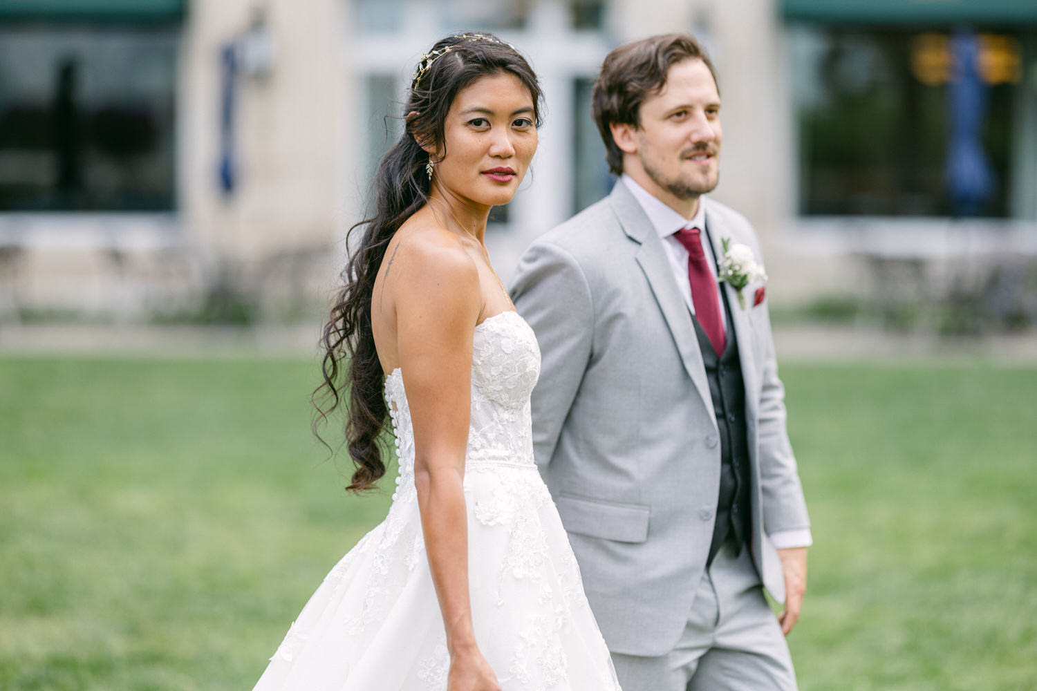 A beautiful bride in a strapless white gown and a groom in a light gray suit, strolling together in an outdoor setting.