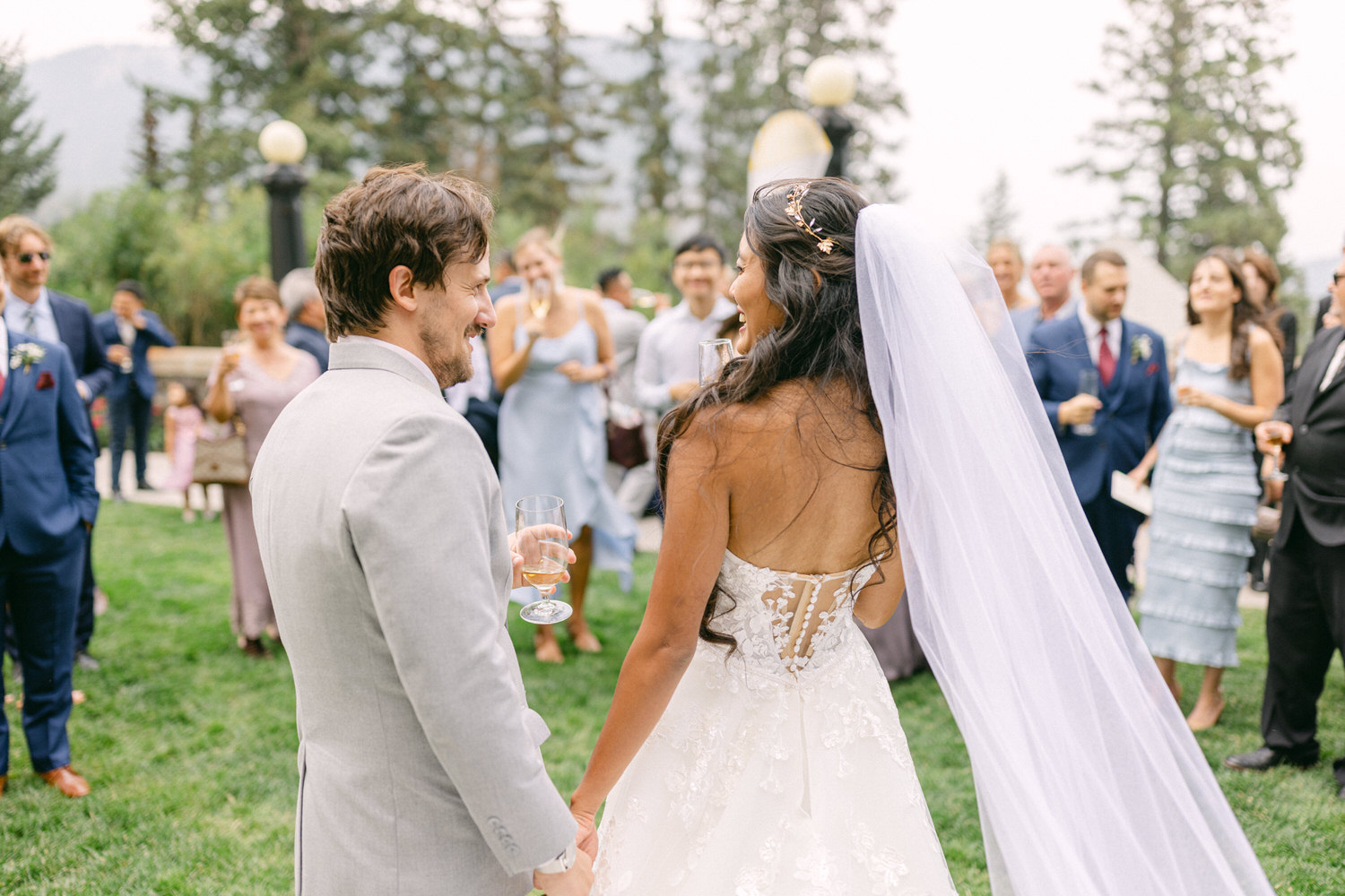 A couple shares a joyful moment during their wedding reception, surrounded by friends and family in a picturesque outdoor setting.