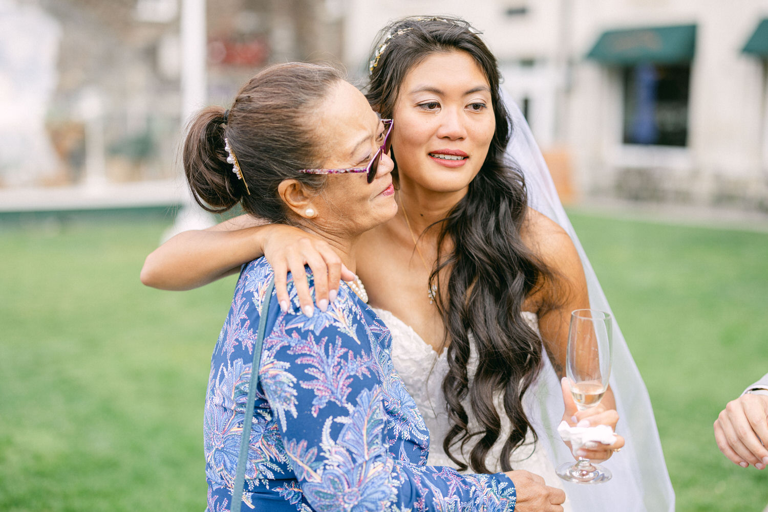 A bride embraces her mother while holding a champagne glass, sharing a heartfelt moment during the wedding celebration.