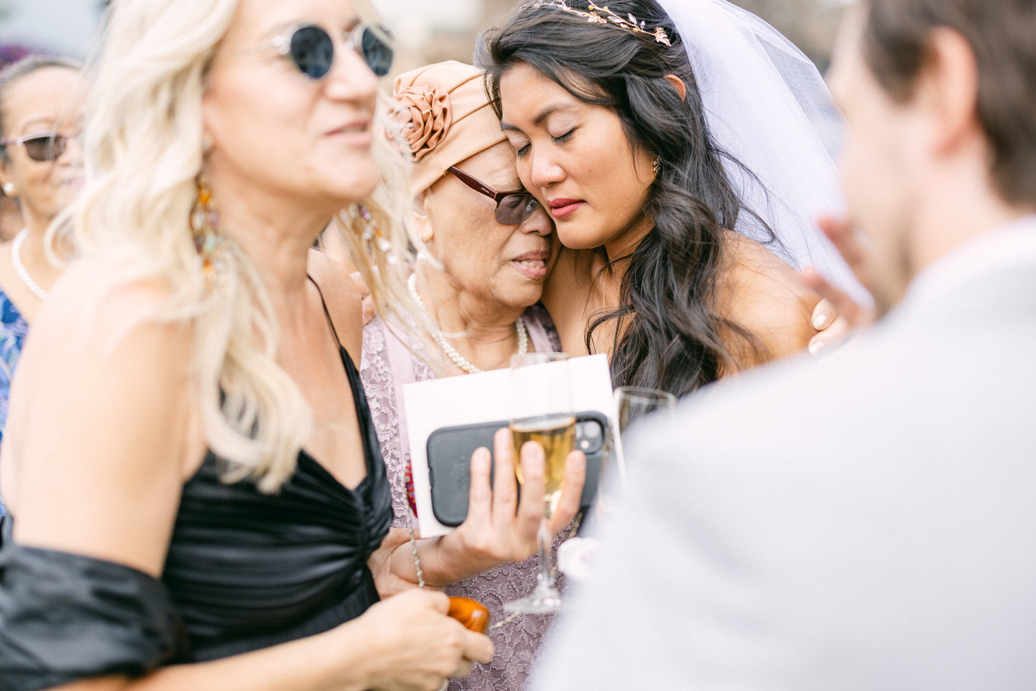 A bride shares a heartfelt moment with her grandmother and friends, surrounded by joy and love during a wedding gathering.