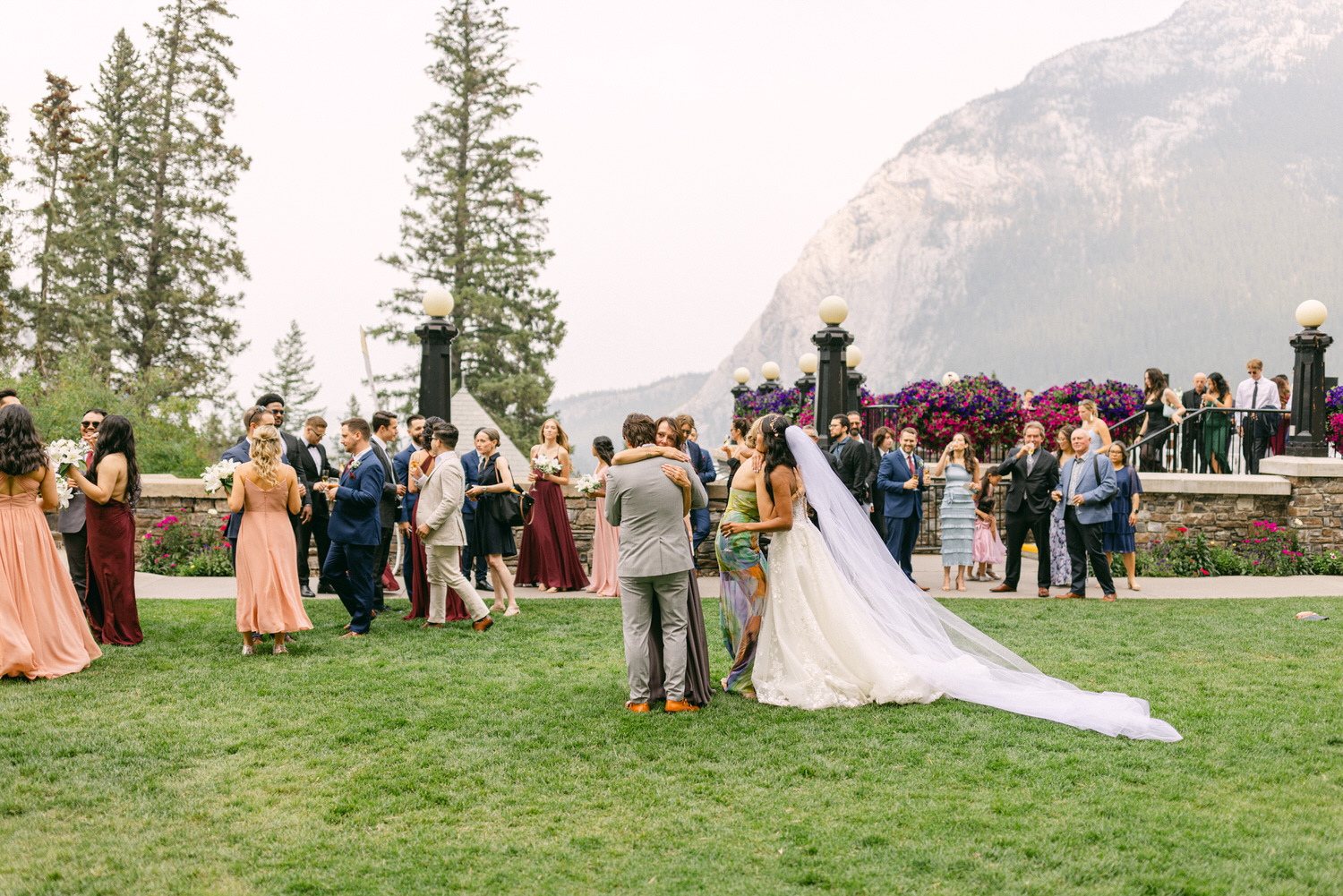 A joyful outdoor wedding scene featuring guests mingling in elegant attire, the bride and groom sharing an intimate moment, surrounded by picturesque mountains and vibrant flowers.