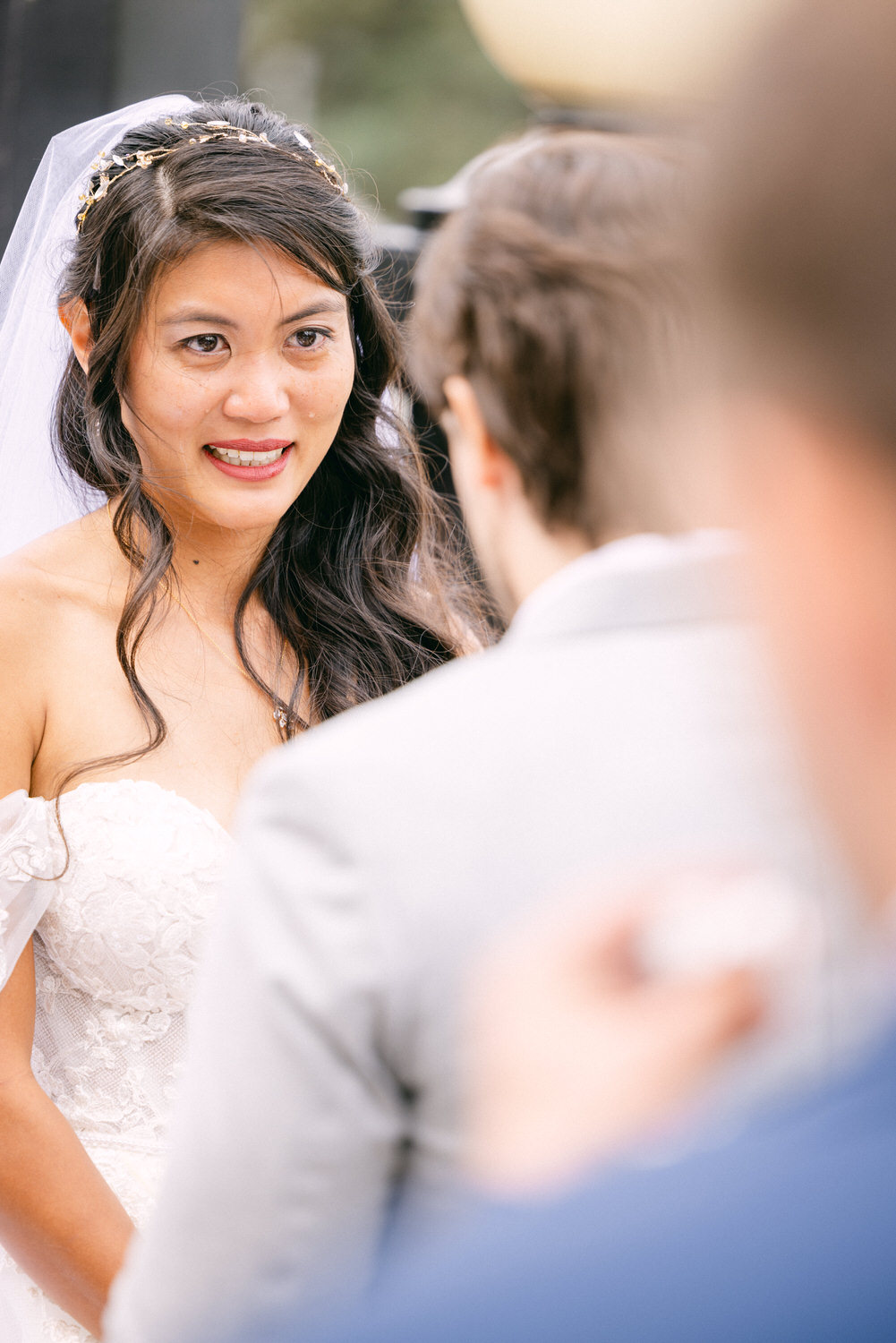 Wedding Vows Exchange::A bride in a stunning lace gown and veil looks earnestly at her partner during a heartfelt moment at their wedding ceremony.