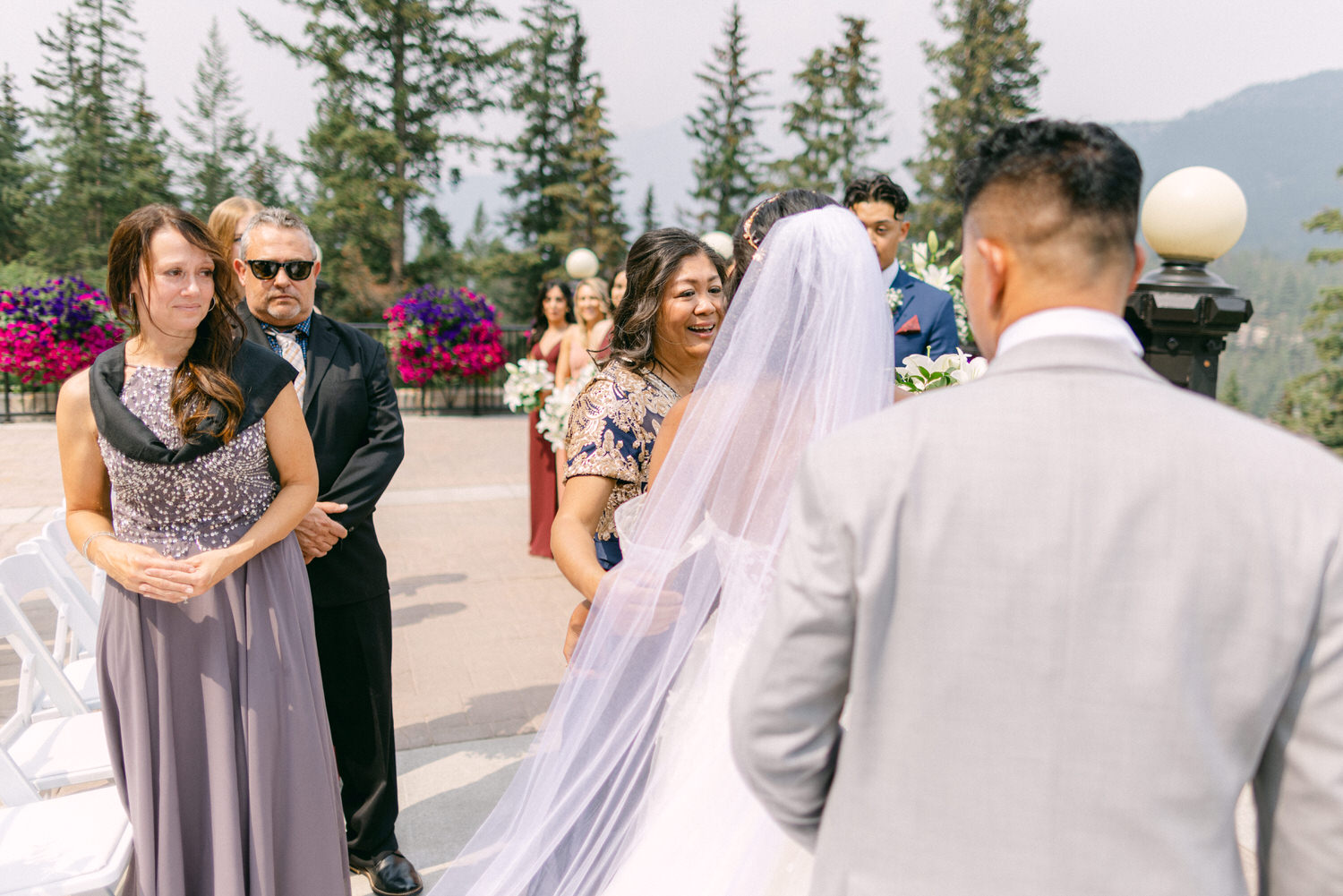 Guests celebrating a bride's arrival at an outdoor wedding, surrounded by floral decorations and scenic mountains.