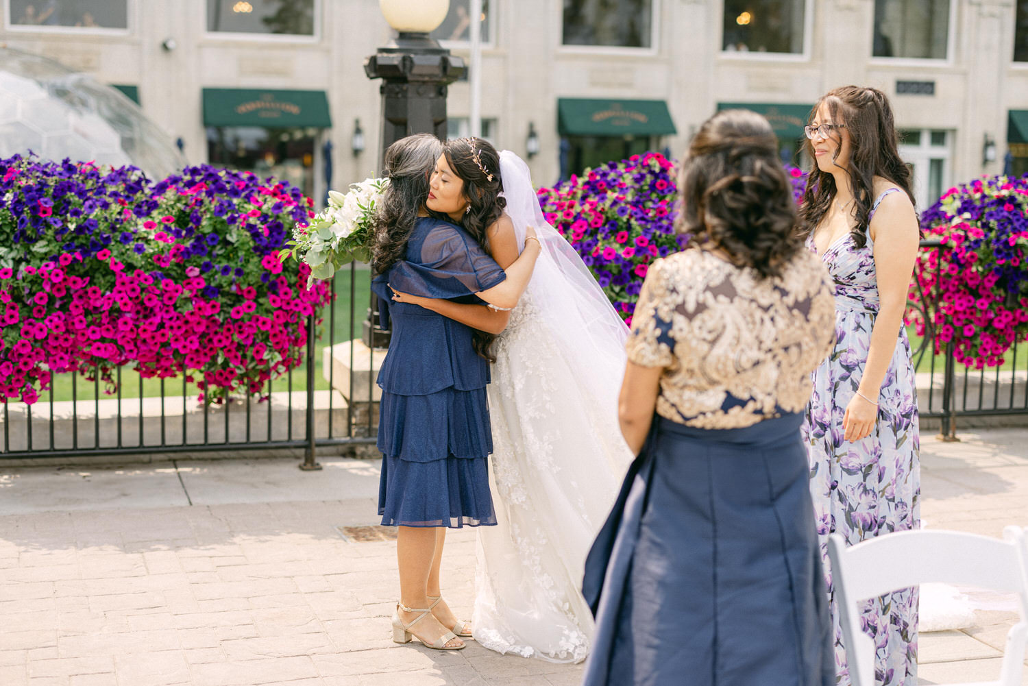 A bride hugs a close friend amidst vibrant flower decorations, capturing a heartfelt moment before the ceremony.