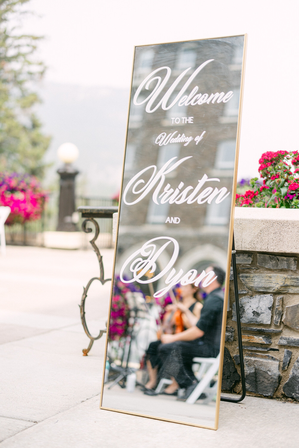 A decorative mirror sign welcoming guests to the wedding of Kristen and Dyon, surrounded by vibrant flowers and outdoor decor.