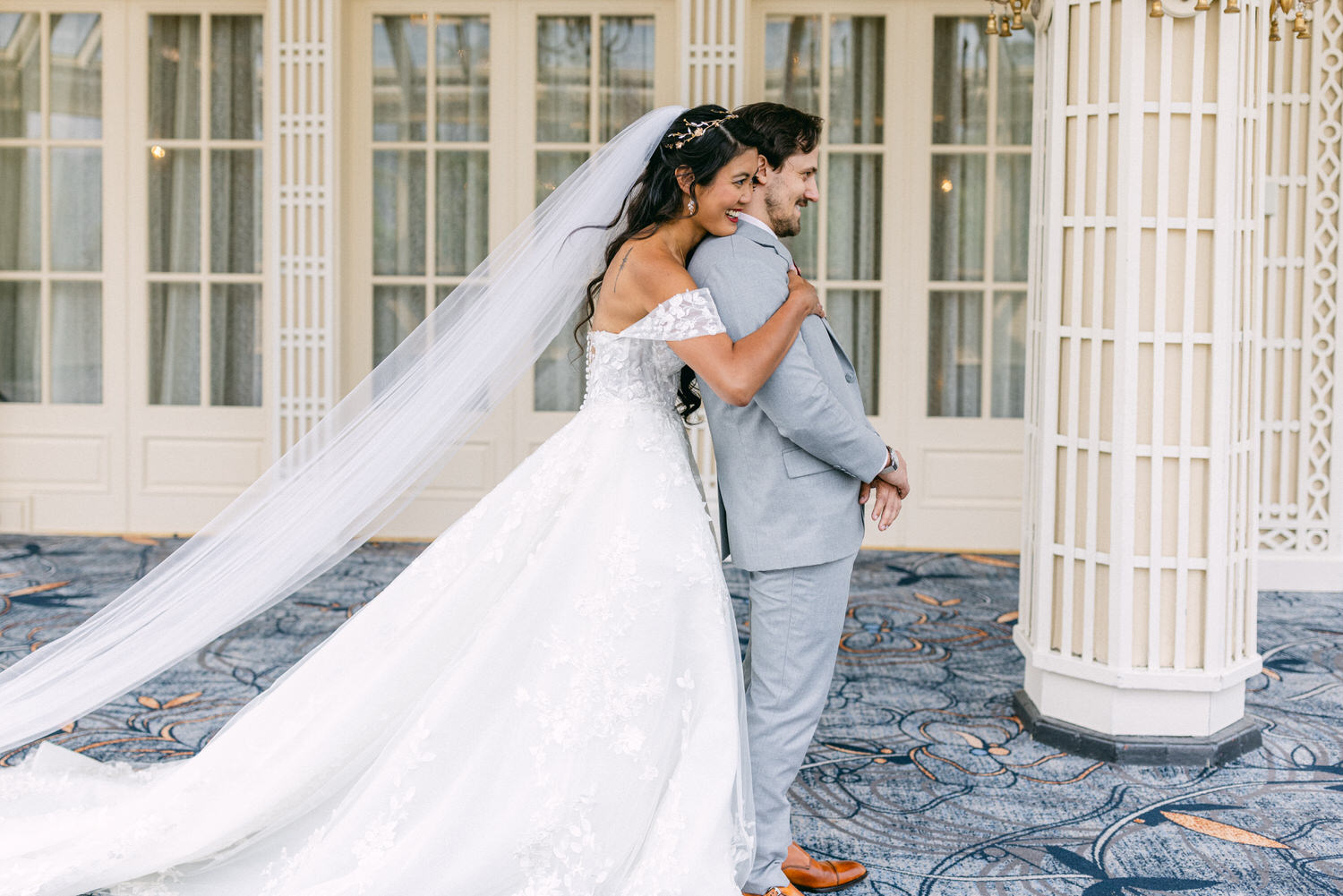 A happy bride playfully hugs her groom from behind, both beaming with joy in a beautifully decorated venue.