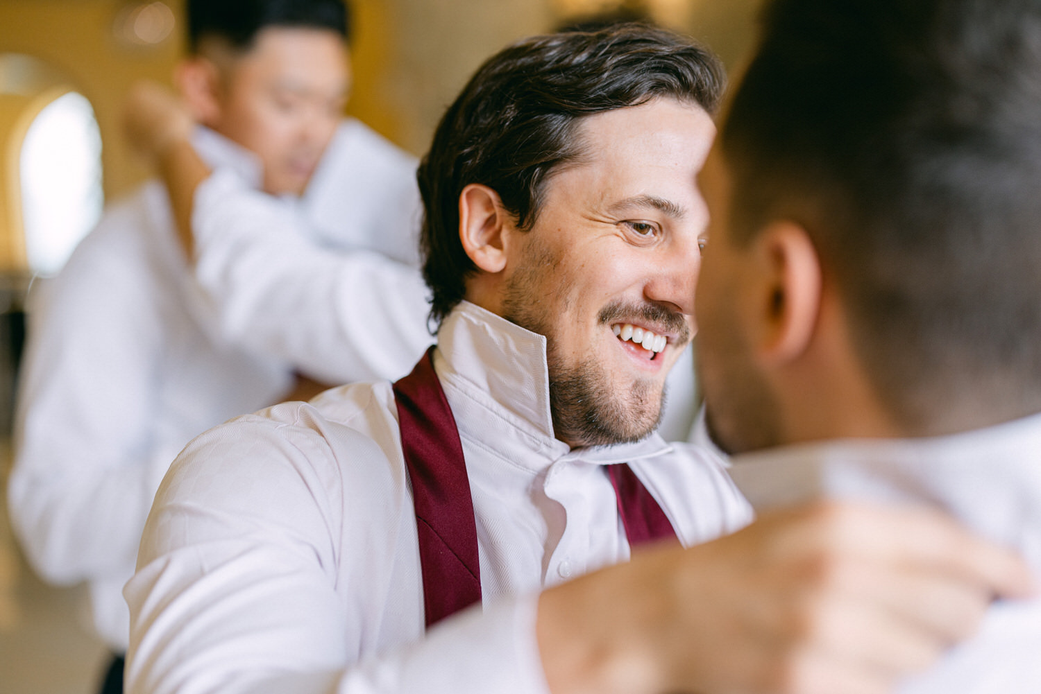 Two groomsmen help each other adjust their formal outfits, showcasing smiles and camaraderie in a stylish setting.