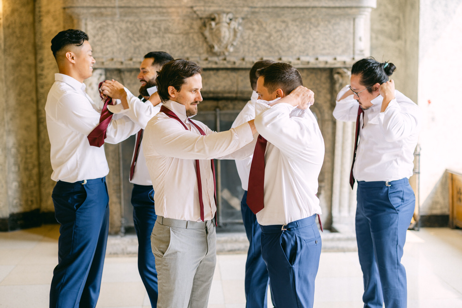 A group of groomsmen helping each other adjust their ties and shirts in a stylish setting before the wedding ceremony.