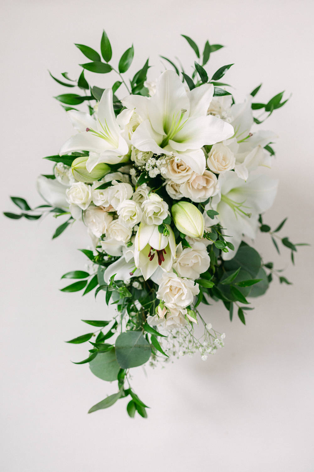 A lush arrangement featuring white lilies, roses, and greenery against a light background.