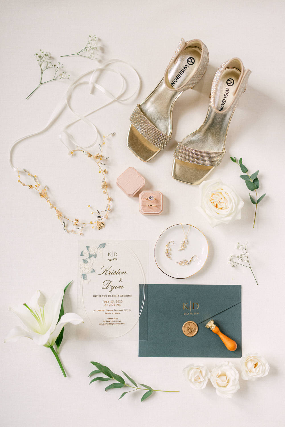 A flat lay arrangement showcasing elegant wedding shoes, floral accessories, invitation card, and jewelry pieces against a soft background.