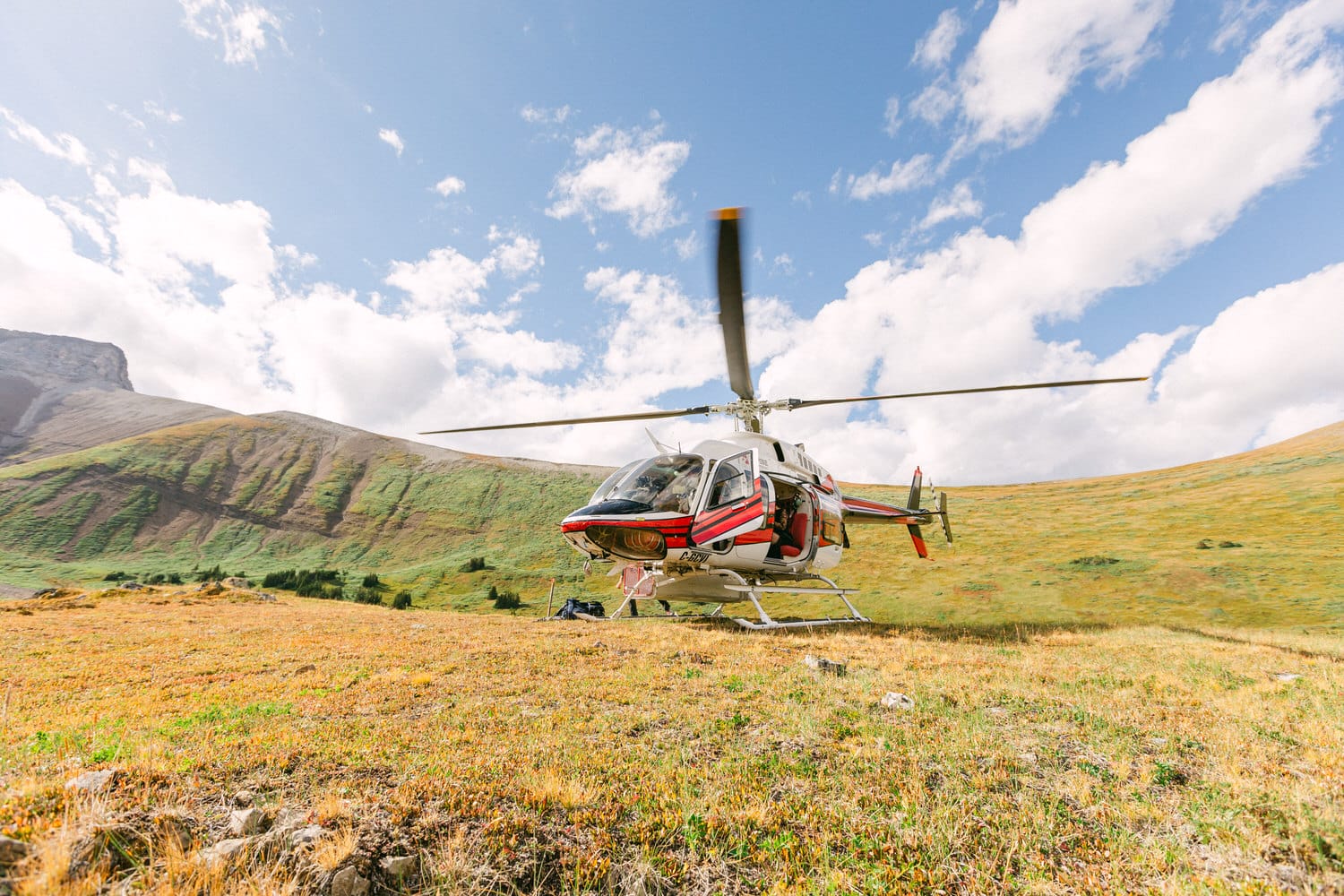 A helicopter parked on a grassy field surrounded by mountains and blue skies.