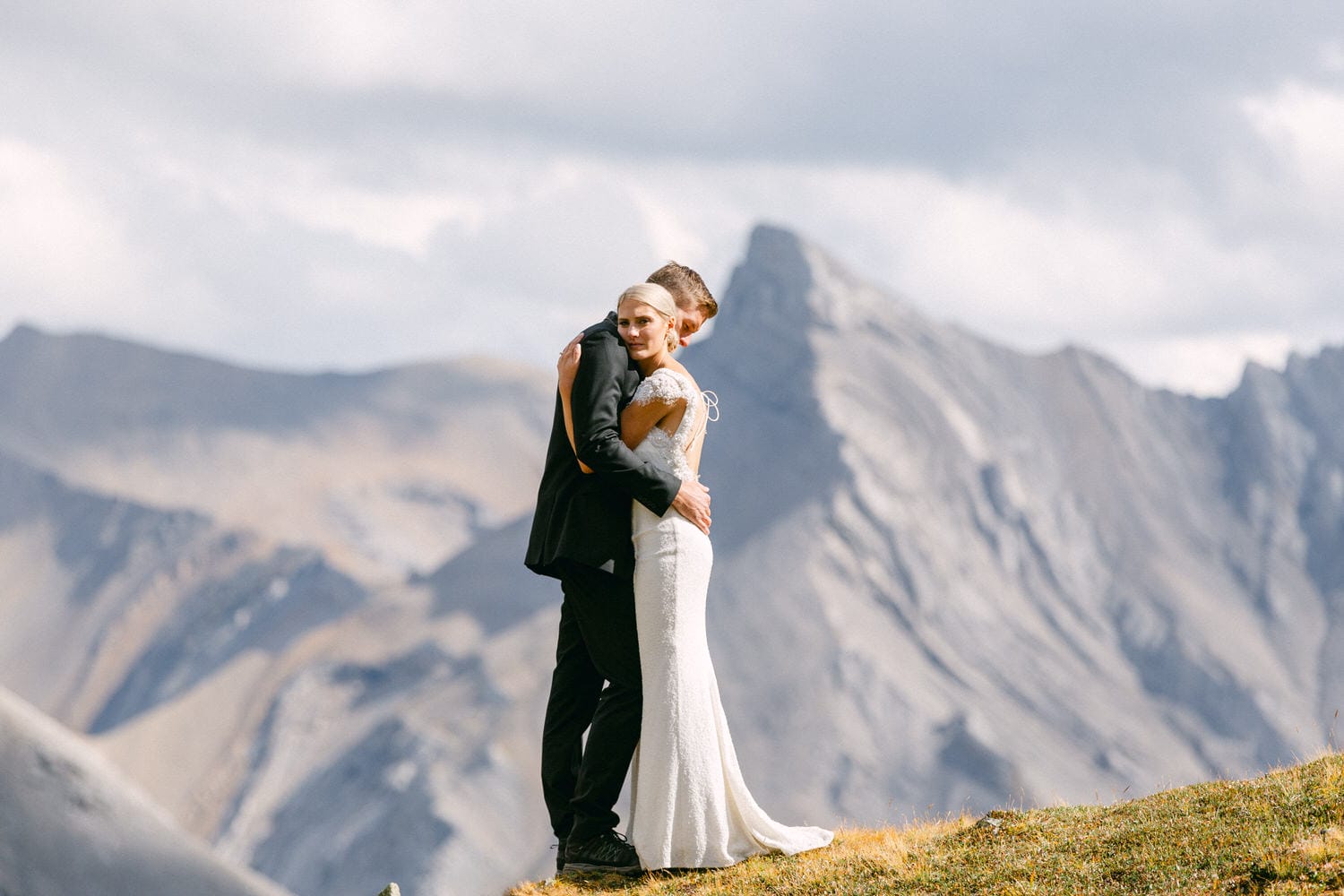 A couple embraces on a mountain ridge, celebrating their wedding in a picturesque, serene landscape with rugged peaks in the background.