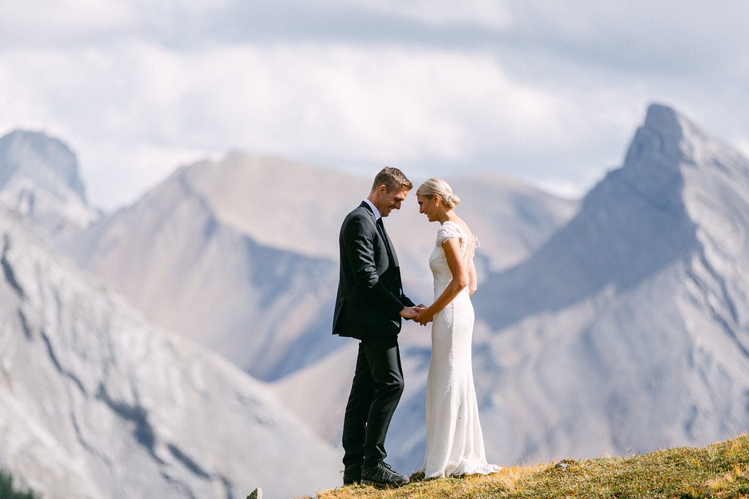 A bride and groom holding hands during their wedding ceremony, set against a stunning mountain backdrop.