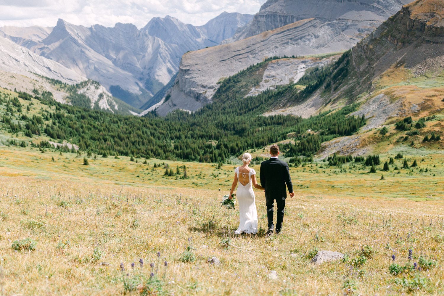 A couple walks hand in hand through a picturesque mountain landscape, celebrating their love against a backdrop of lush greenery and towering peaks.