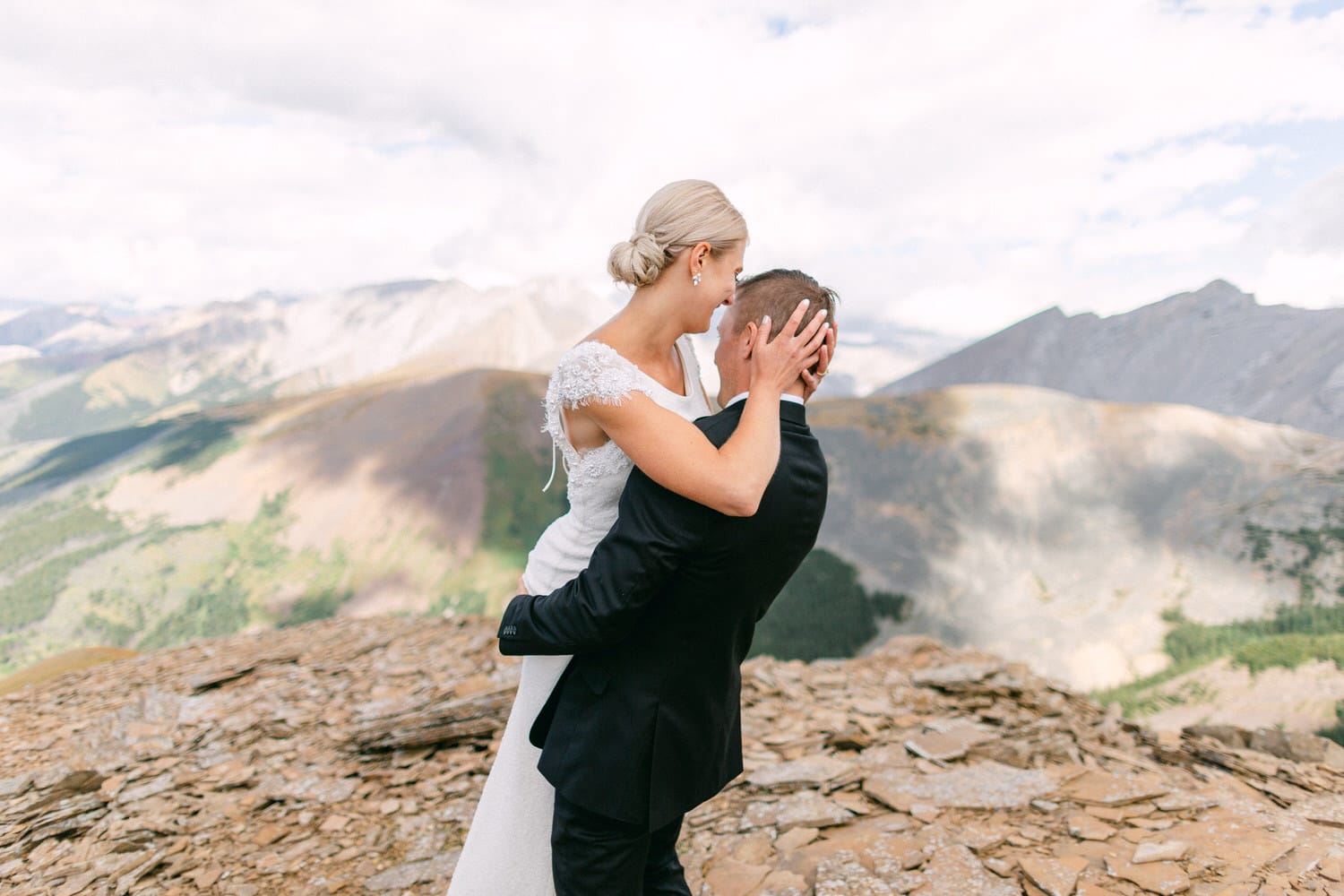 A joyful couple embracing during their wedding celebration atop a scenic mountain landscape.