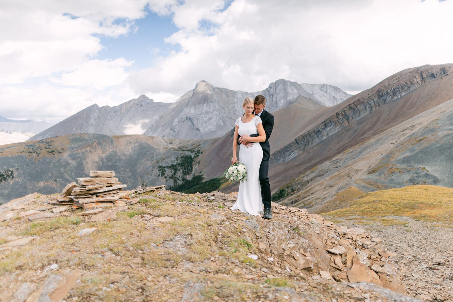 A couple embraces on a rocky overlook surrounded by majestic mountains, capturing a serene wedding moment.