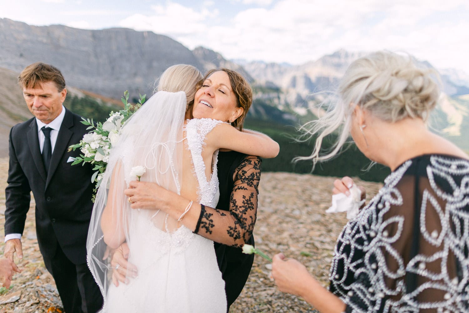 A bride hugs her mother during an emotional moment, surrounded by family and breathtaking mountain scenery.