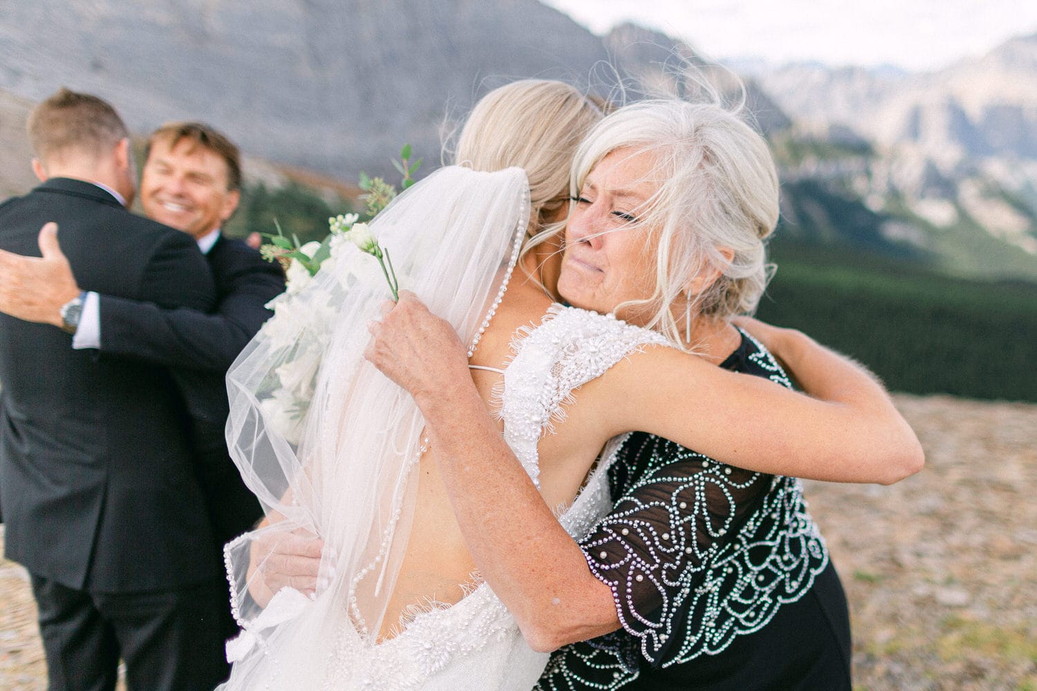 A bride embraces her mother during an intimate moment at a scenic outdoor wedding, surrounded by mountains and greenery.