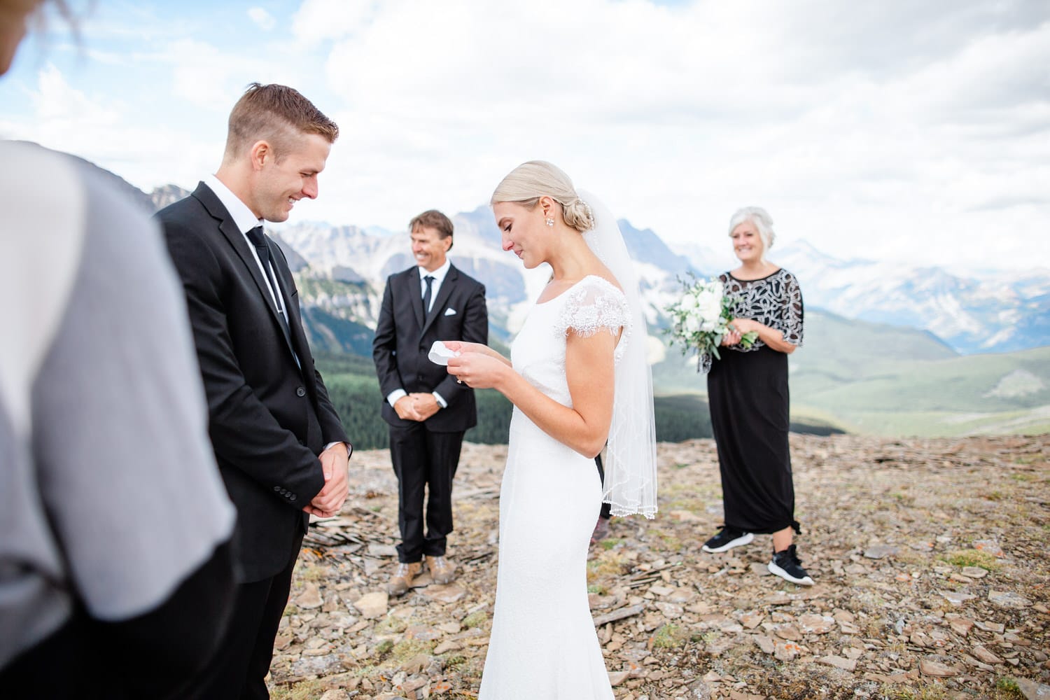 A beautiful outdoor wedding ceremony with the bride and groom exchanging vows against a stunning mountain backdrop, surrounded by family and friends.