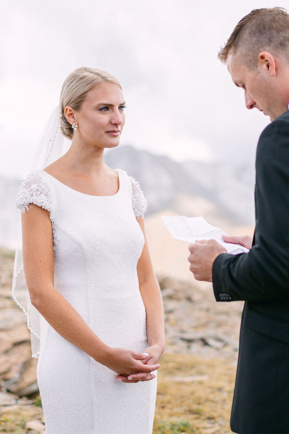 Bride listening attentively during an outdoor wedding ceremony, with a groom reading vows.