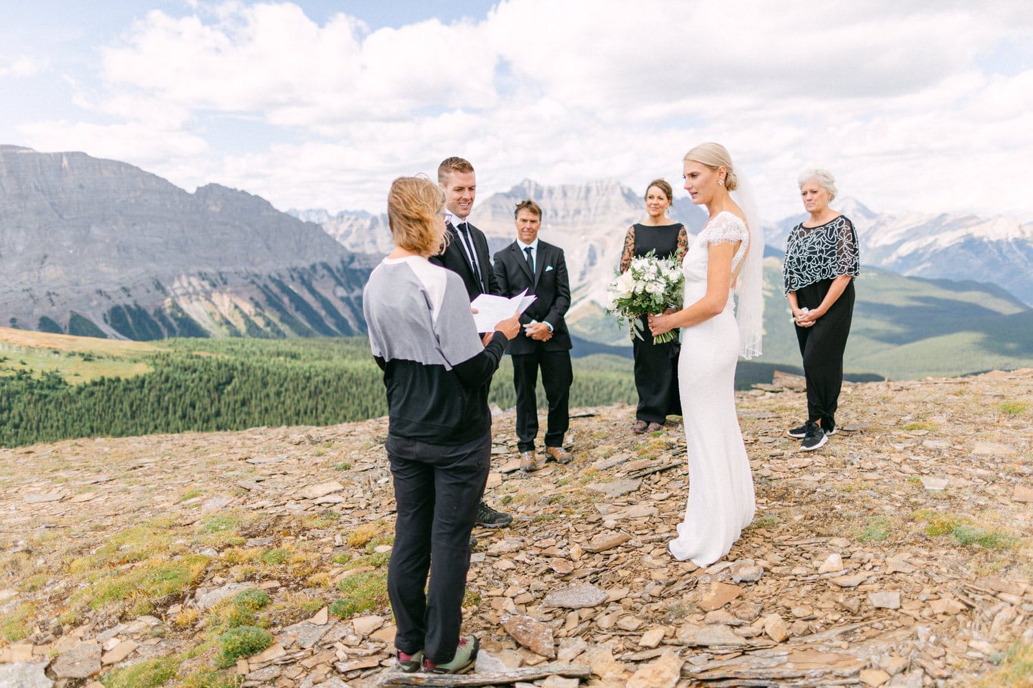 An intimate wedding ceremony in a stunning mountainous landscape, with the bride and groom surrounded by family and a celebrant.